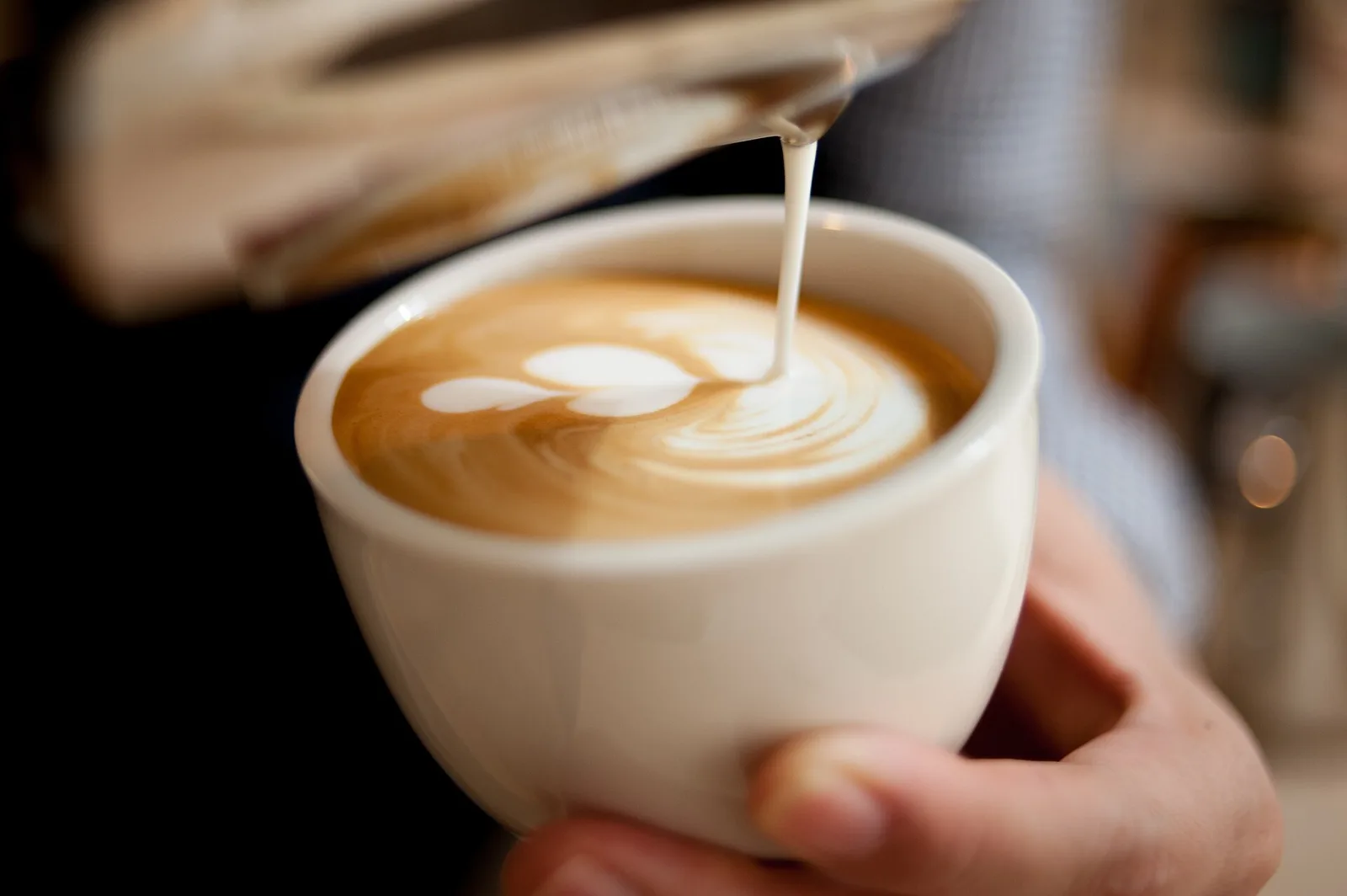 A barista pours steamed milk into a cup of coffee to make latte art.