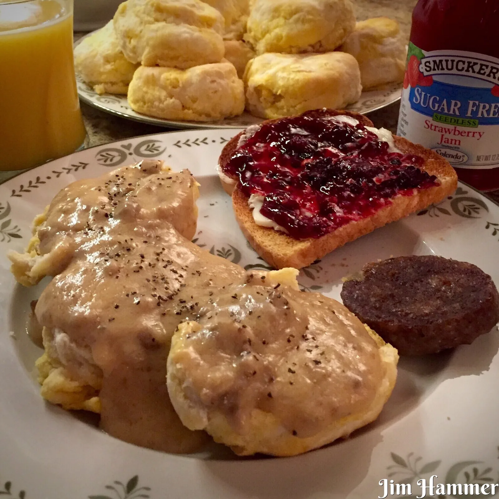 Biscuits and sausage gravy with toast, strawberry jam and orange juice on a breakfast table