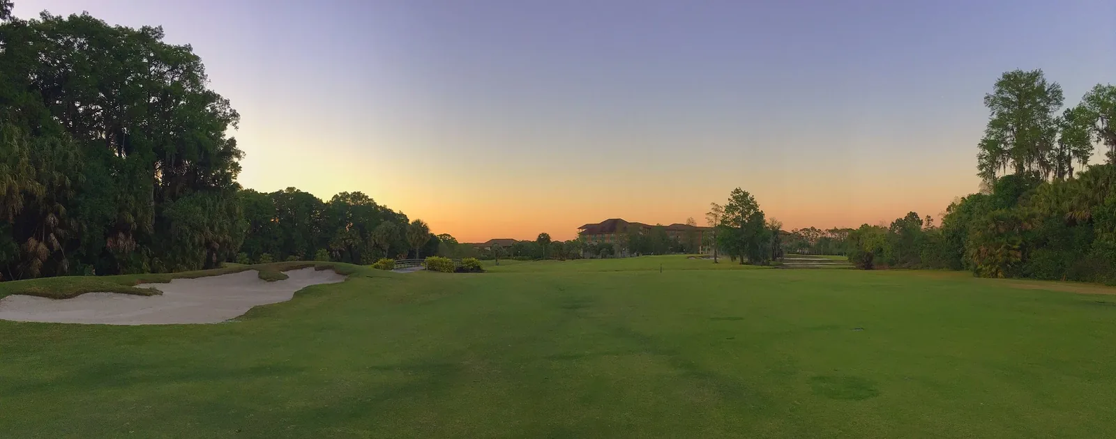 A golf fairway and sand bunker at sunset, lined with trees