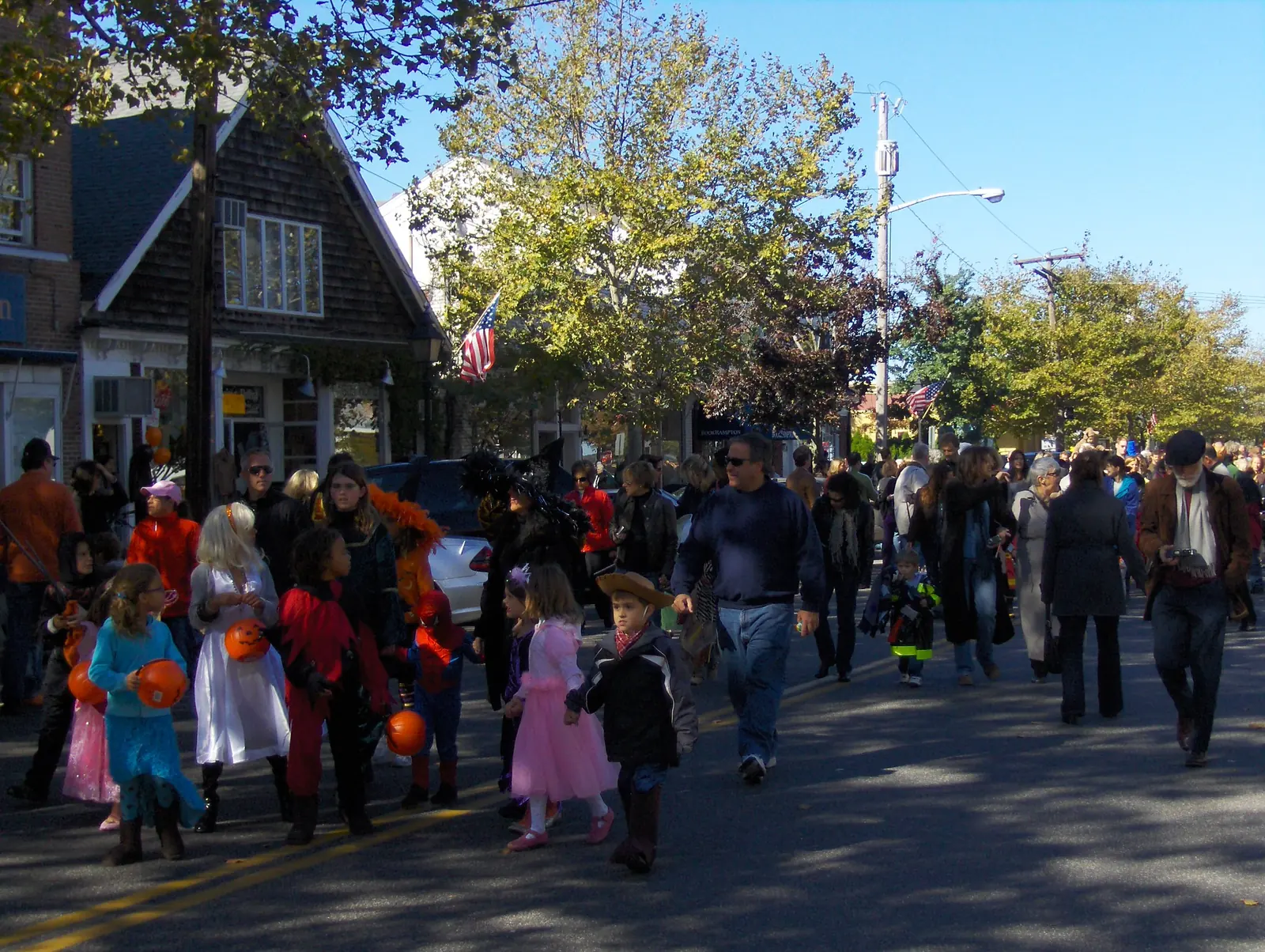 Children in Halloween costumes walk down a village main street in a community Halloween parade