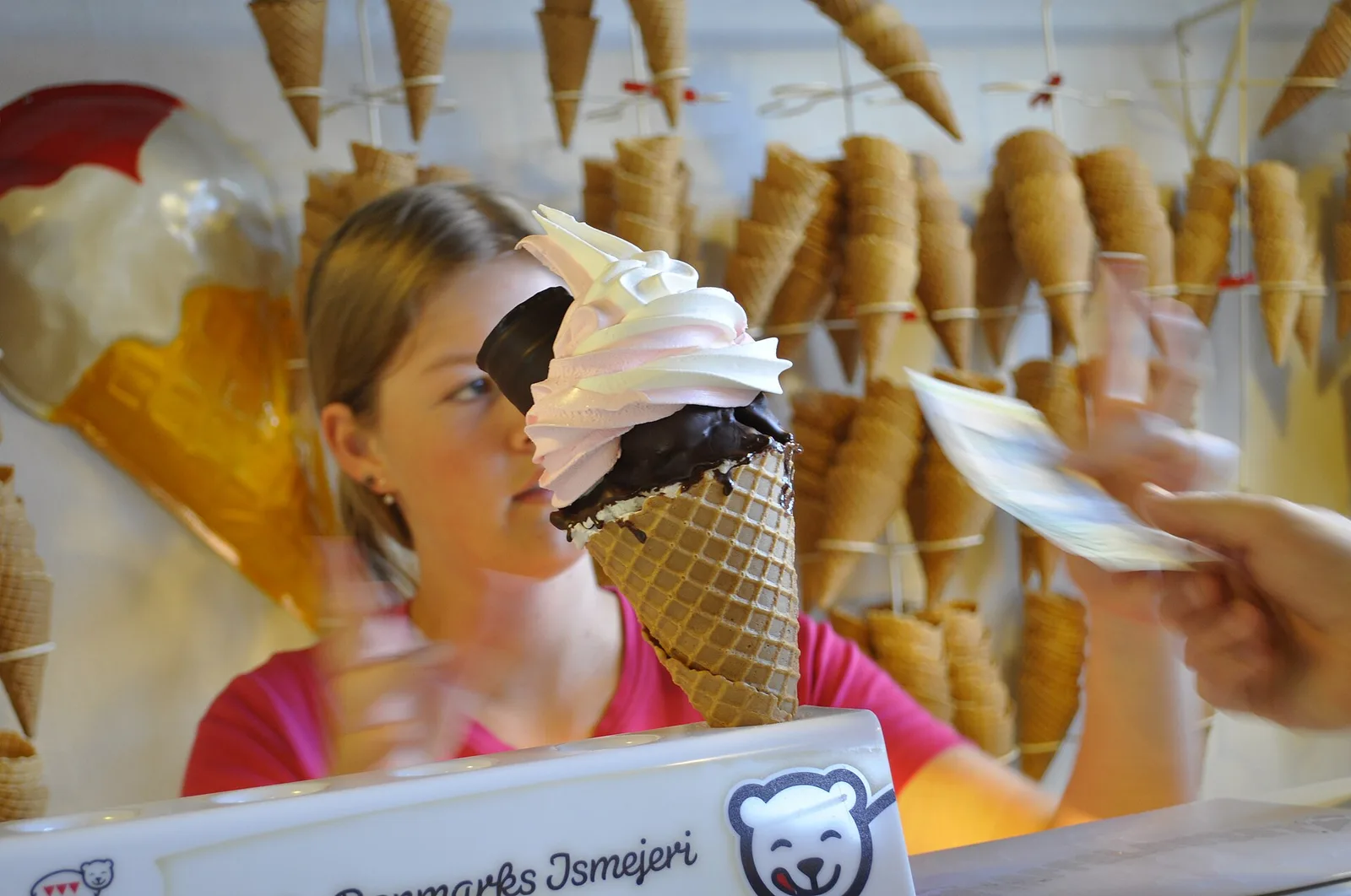 A soft-serve ice cream in a waffle cone handed across the counter at an ice cream shop.