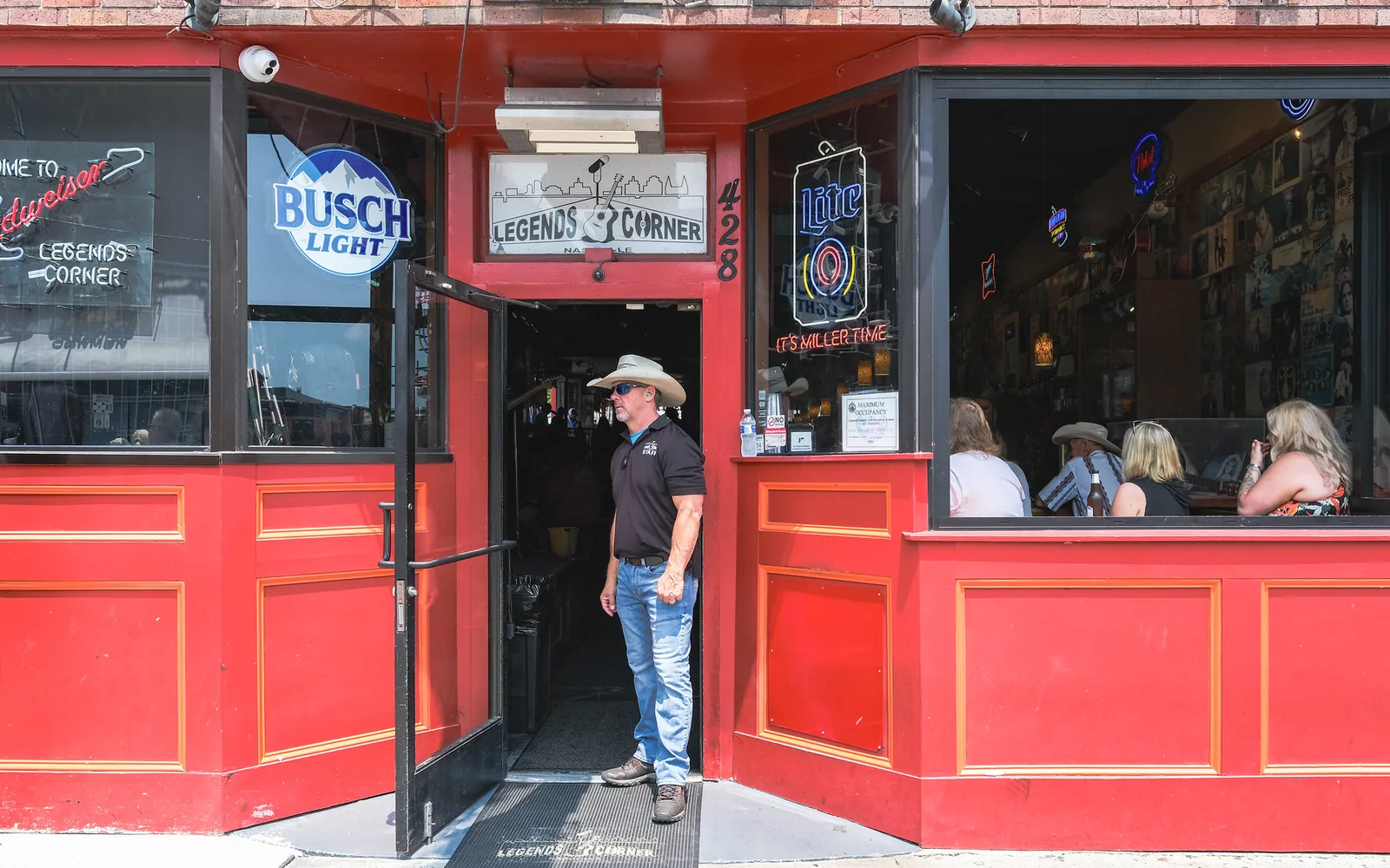 A doorman in a cowboy hat stands at the open door of Legends Corner, a honky-tonk in Nashville