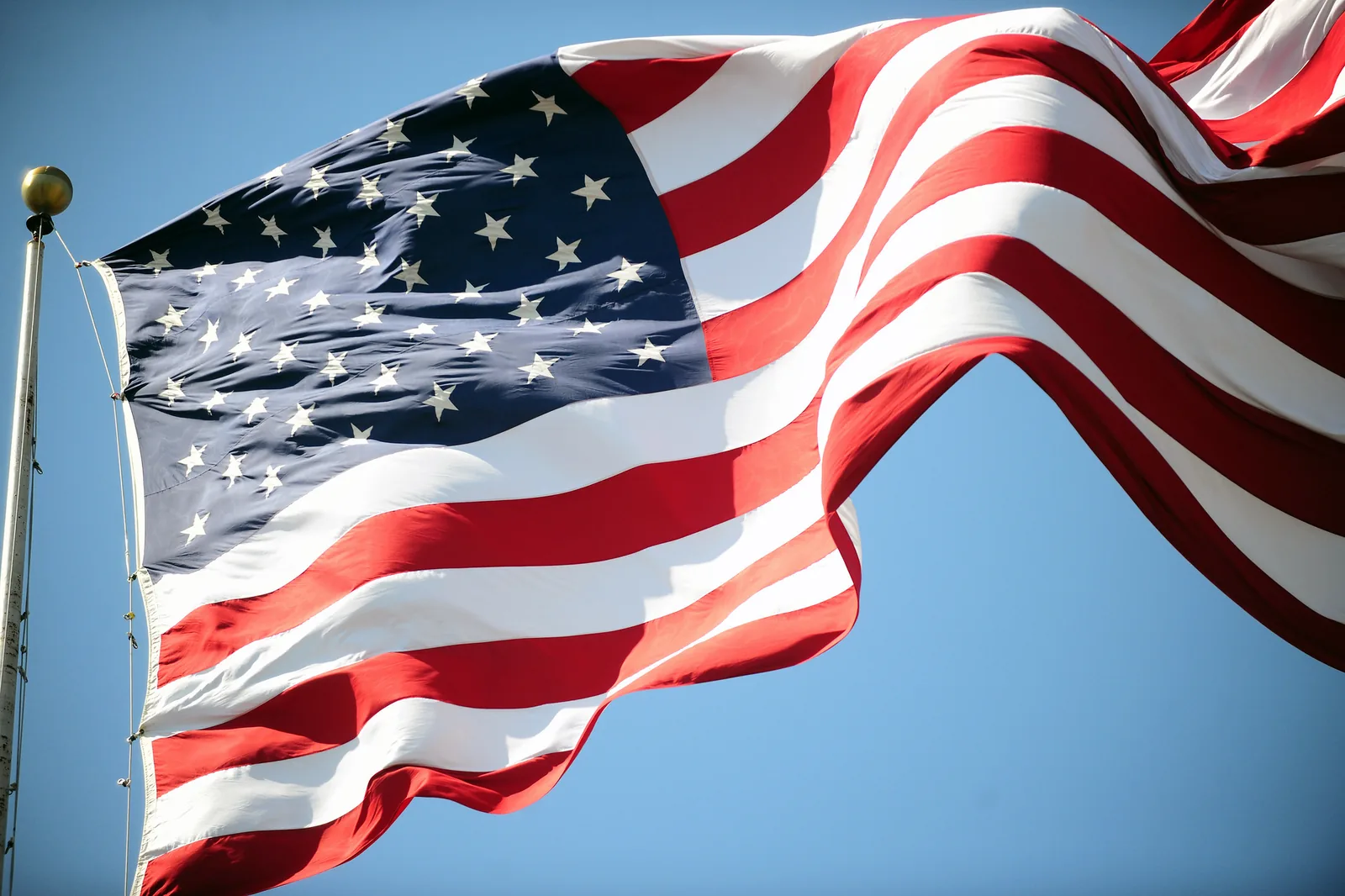 An American flag flies against a clear sky at a Memorial Day ceremony