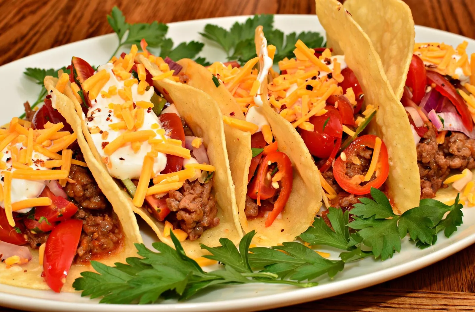 A plate of crisp tacos topped with cheese, tomato and peppers.