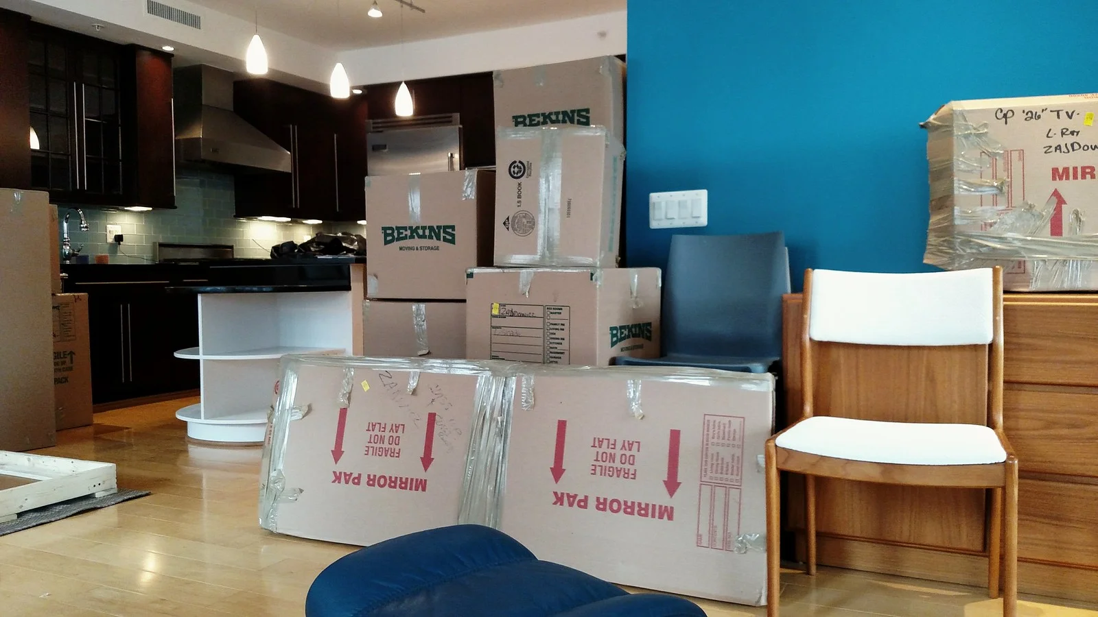 Packed moving boxes, a wrapped mirror and chairs stacked in a new home's kitchen and living room