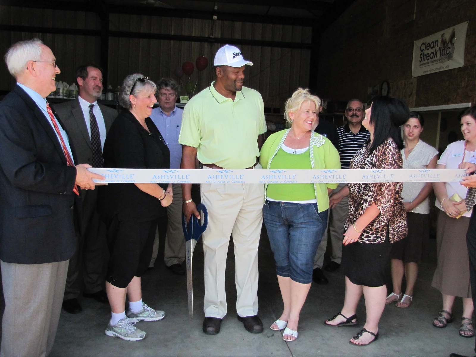 Business owners and chamber members cut a ribbon with giant scissors at a chamber of commerce ribbon cutting in Asheville, North Carolina