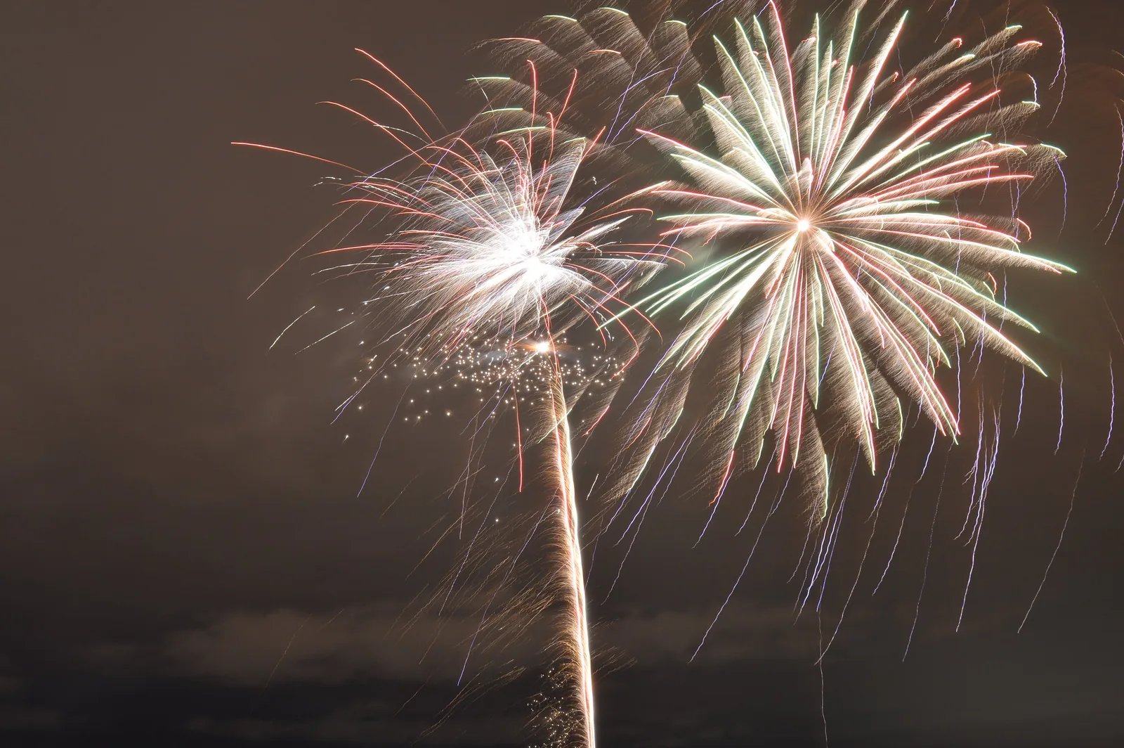 Two fireworks shells burst in white and green over a dark sky on New Year's Eve