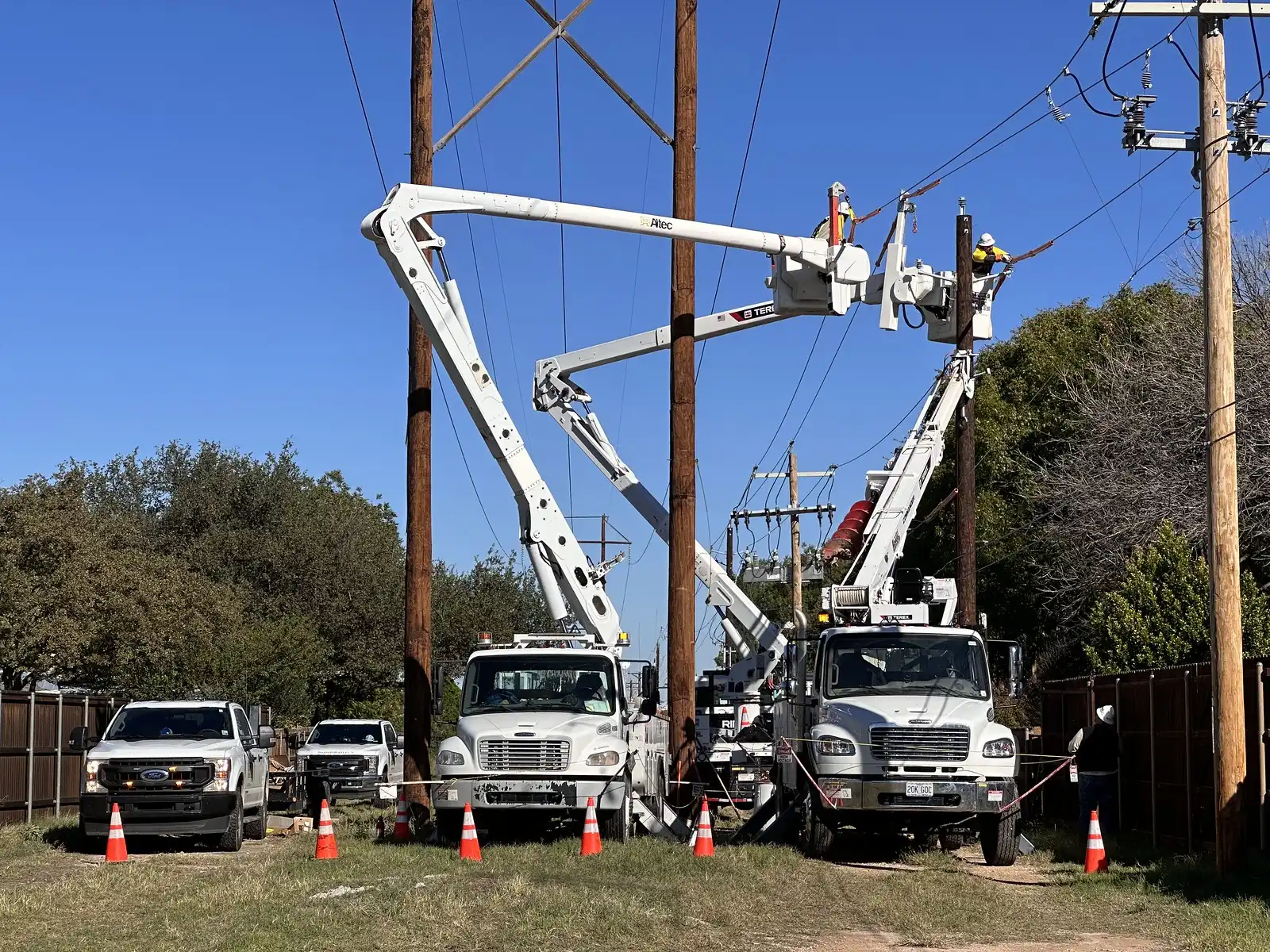 Linemen in two bucket trucks replace a utility pole and transformer beside a residential street