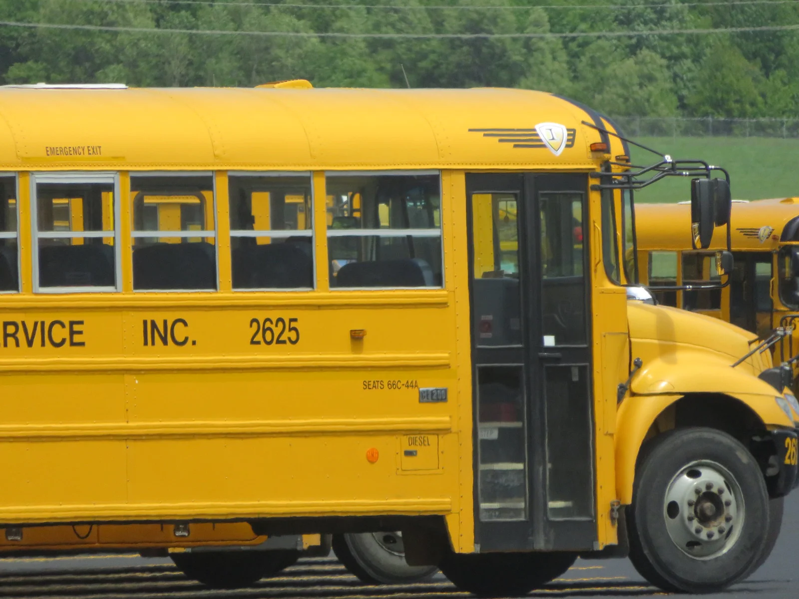 A yellow school bus parked at a bus contractor's lot, with a second bus behind it