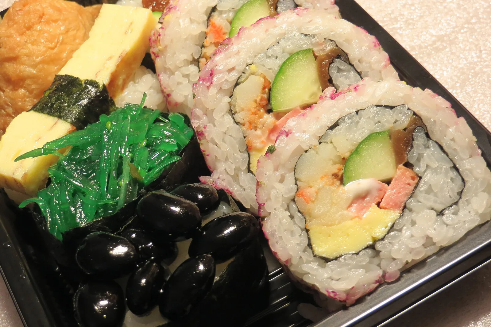 Sushi rolls with cucumber, egg and seaweed salad in a takeout tray.