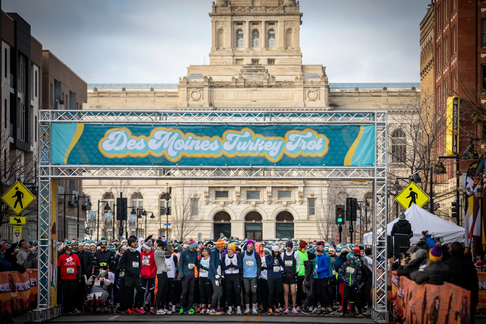 Runners in hats and costumes pack the start line under an inflatable arch at a Thanksgiving turkey trot