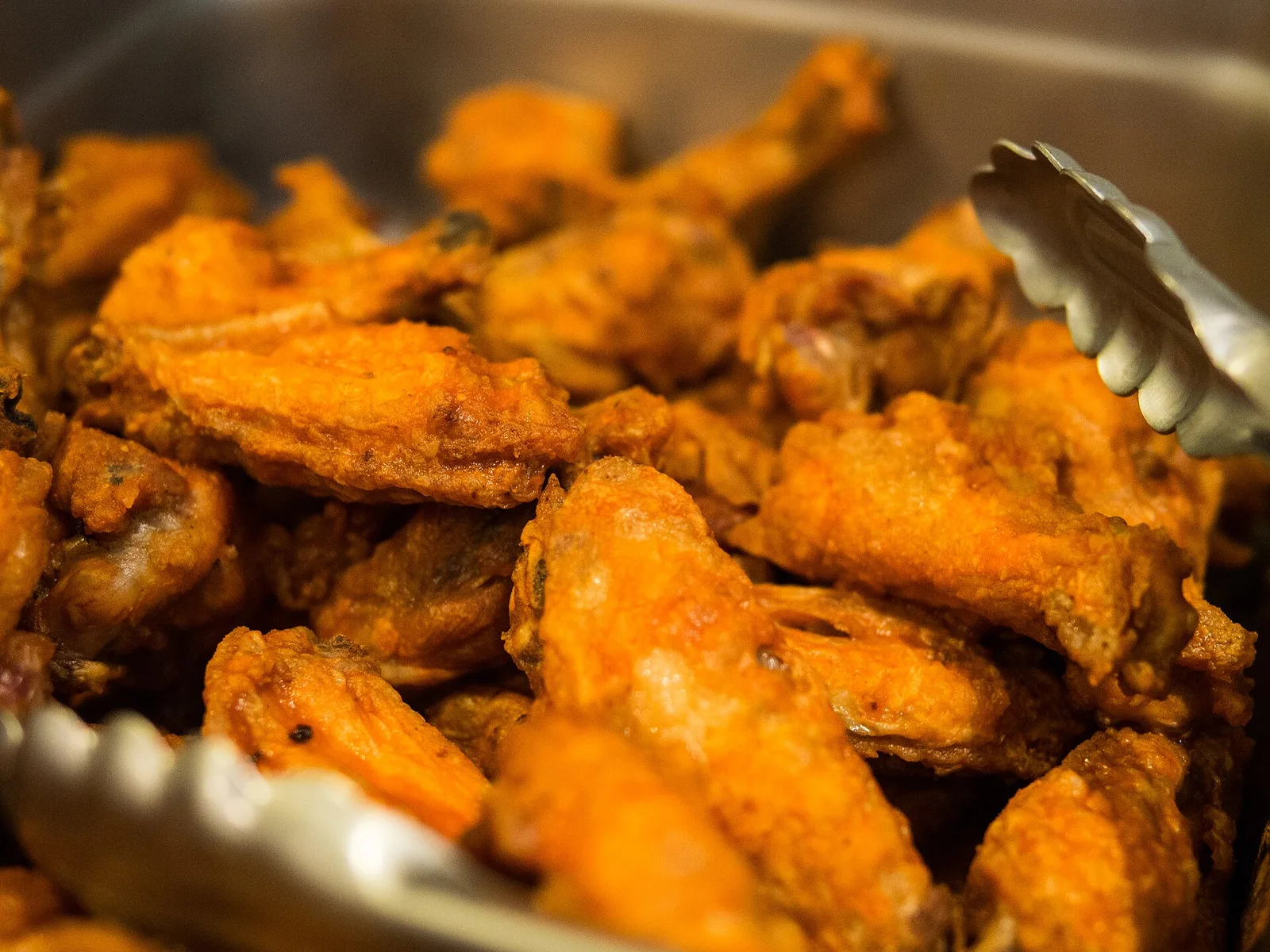 A tray of Buffalo-style chicken wings with serving tongs.